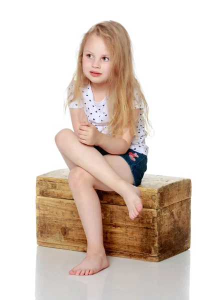 A little girl is sitting on a wooden box. — Stock Photo, Image