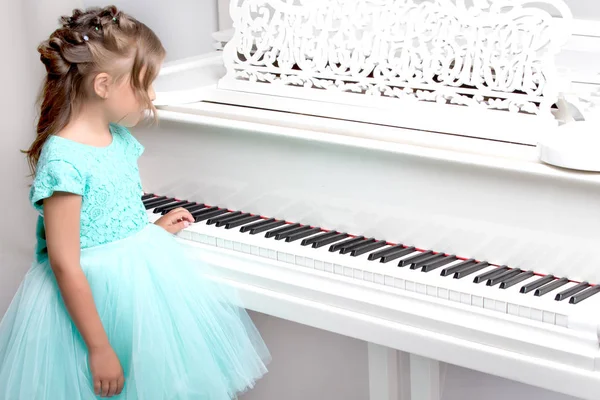 Menina bonita está tocando em um piano de cauda branco. — Fotografia de Stock