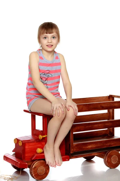La chica está sentada en un gran coche de madera de juguete . —  Fotos de Stock
