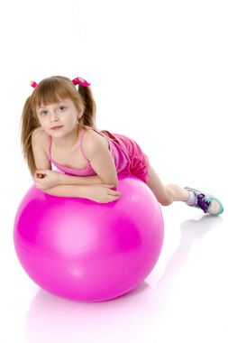 Küçük kız spor yapmak için büyük bir top üzerinde egzersiz yapıyor..
