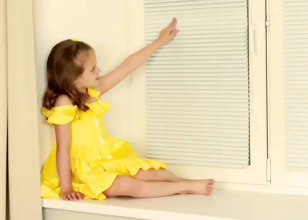 A little girl is sitting by the window with jalousie — Stock Photo, Image