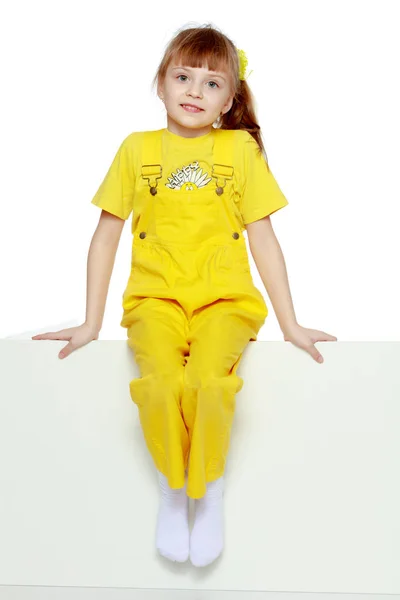 Chica con un flequillo corto en la cabeza y un mono amarillo brillante . — Foto de Stock