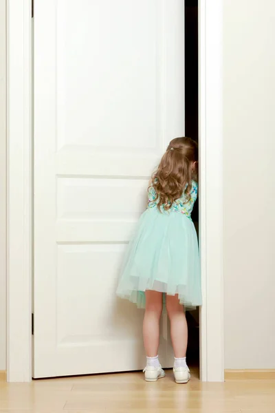 Een klein meisje staat door de deur. — Stockfoto
