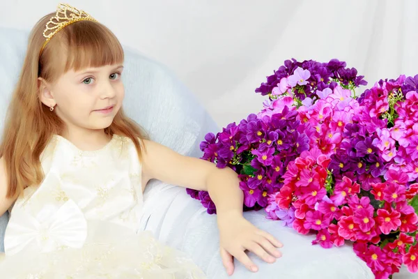 Menina senta-se ao lado de um buquê de flores . — Fotografia de Stock