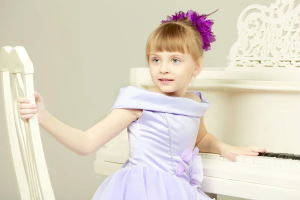 Uma menina está posando perto de um piano de cauda branco . — Fotografia de Stock