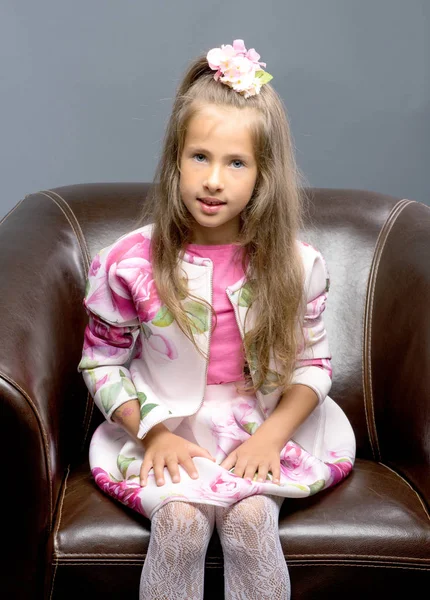 Ένα κοριτσάκι κάθεται σε μια δερμάτινη καρέκλα. — Φωτογραφία Αρχείου