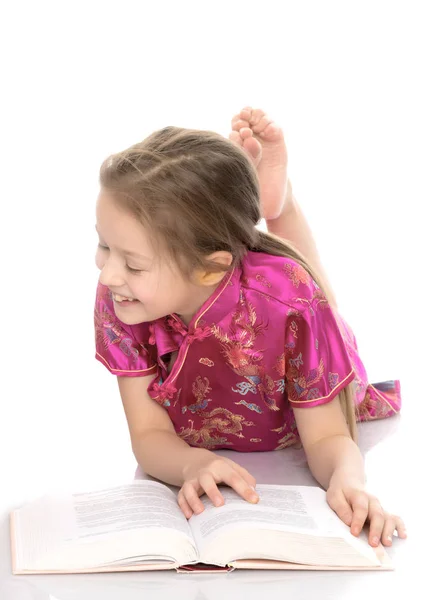 Ein kleines Mädchen liegt auf dem Boden und liest ein Buch. — Stockfoto