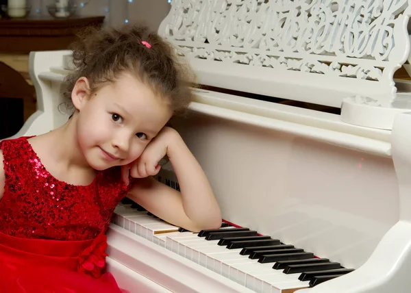 Beautiful little girl is playing on a white grand piano. — Stock Photo, Image