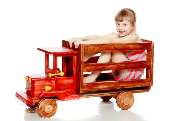 Das Mädchen sitzt auf einem großen Spielzeugauto aus Holz. — Stockfoto