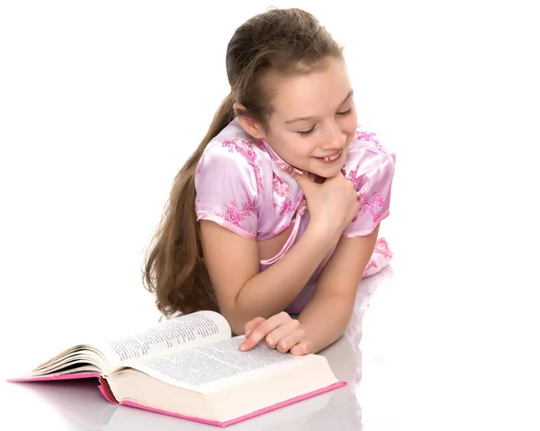 Uma menina está deitada no chão lendo um livro . — Fotografia de Stock