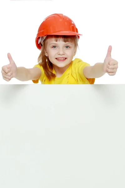 Girl in a construction helmet peeks out from behind a billboard. — Stock Photo, Image