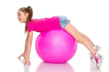 Küçük kız spor yapmak için büyük bir top üzerinde egzersiz yapıyor..