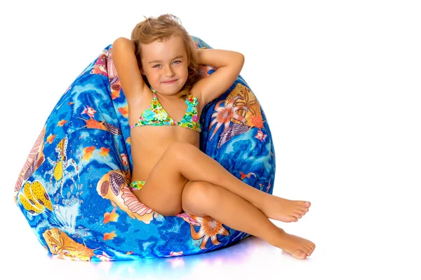 Little girl in a swimsuit is sitting on a pillow. — Stock Photo, Image