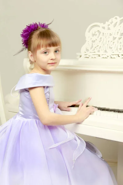 Uma menina está posando perto de um piano de cauda branco . — Fotografia de Stock