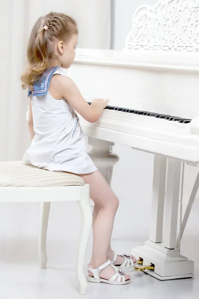 Menina bonita está tocando em um piano de cauda branco. — Fotografia de Stock