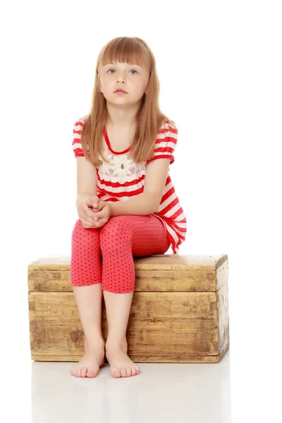 Une petite fille est assise sur une boîte en bois. — Photo