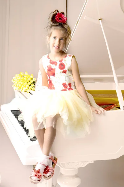 En vacker liten flicka spelar på en vit flygel. — Stockfoto