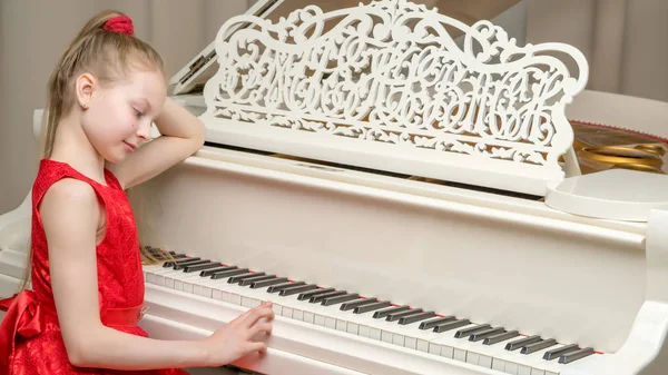 Beautiful little girl is playing on a white grand piano.