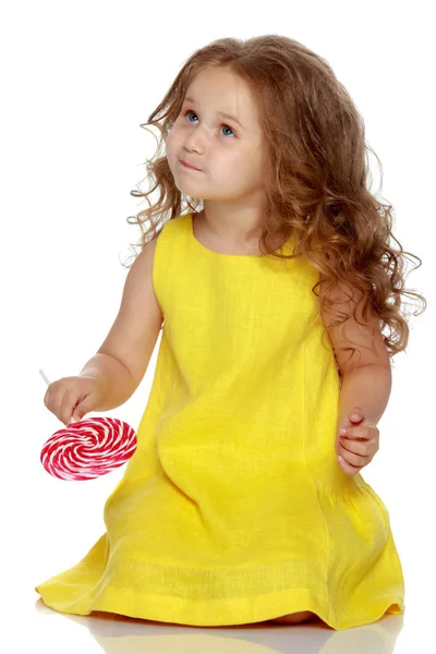 A little girl licks a candy on a stick. Stock Picture