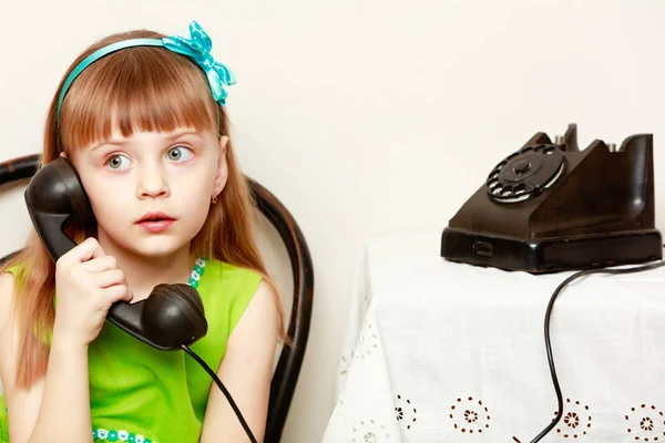 The girl is talking on a black, old phone with a spinning disc. — Stock Photo, Image