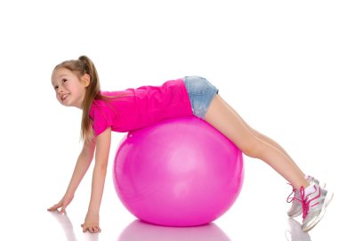 Küçük kız spor yapmak için büyük bir top üzerinde egzersiz yapıyor..