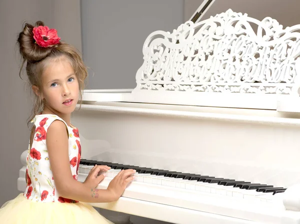 Beautiful little girl is playing on a white grand piano.