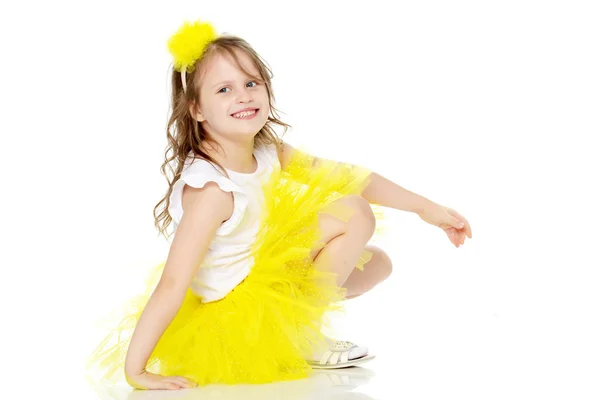 Liten flicka i en gul kjol sitter på golvet. — Stockfoto