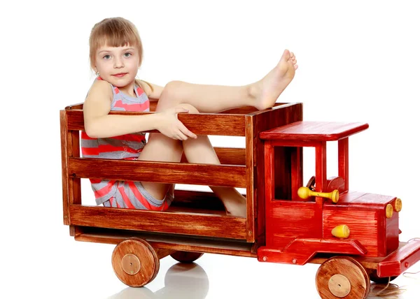 Das Mädchen sitzt auf einem großen Spielzeugauto aus Holz. — Stockfoto