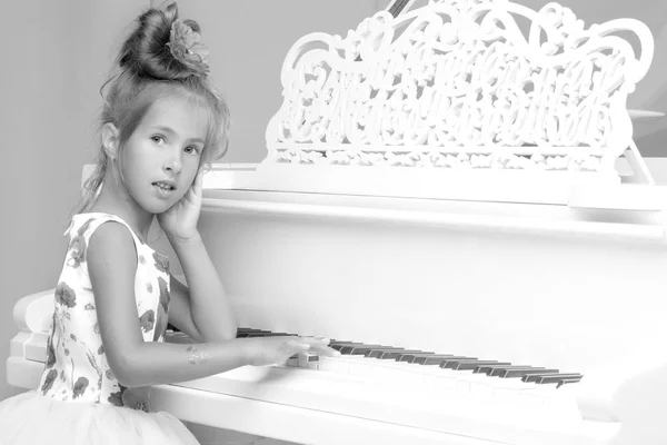 Menina bonita está tocando em um piano de cauda branco. — Fotografia de Stock