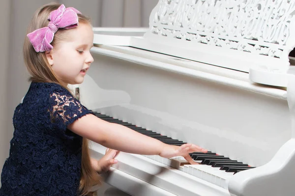아름다운 작은 소녀가 흰색 그랜드 피아노로 연주하고 있습니다.. — 스톡 사진