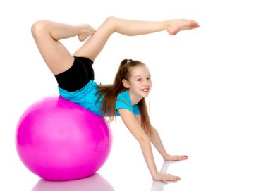 Küçük kız spor yapmak için büyük bir top üzerinde egzersiz yapıyor..