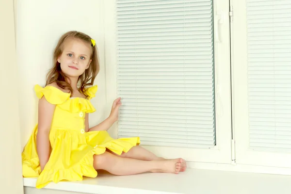 Malá holka sedí u okna v žaluzie — Stock fotografie
