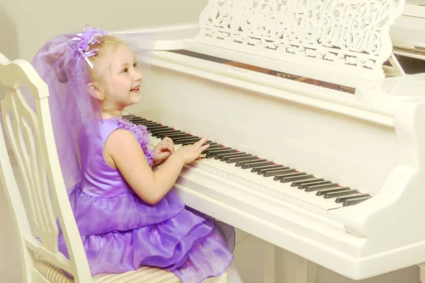 Menina está tocando em um piano de cauda branco . — Fotografia de Stock