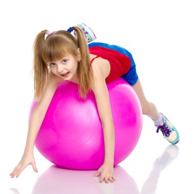 Küçük kız spor yapmak için büyük bir top üzerinde egzersiz yapıyor..