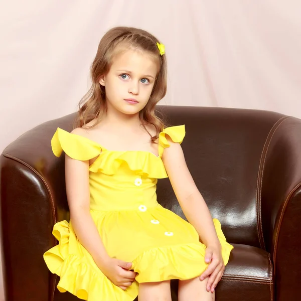 Ein kleines Mädchen sitzt auf einem Lederstuhl. — Stockfoto