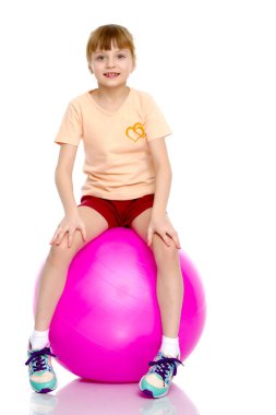 Küçük kız spor yapmak için büyük bir top üzerinde egzersiz yapıyor..