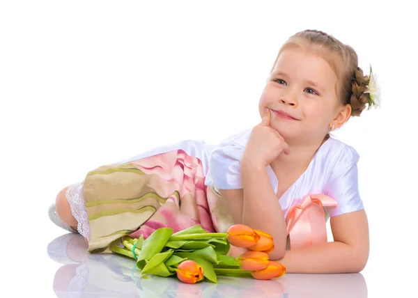 Une petite fille est allongée sur le sol avec un bouquet de tulipes . — Photo