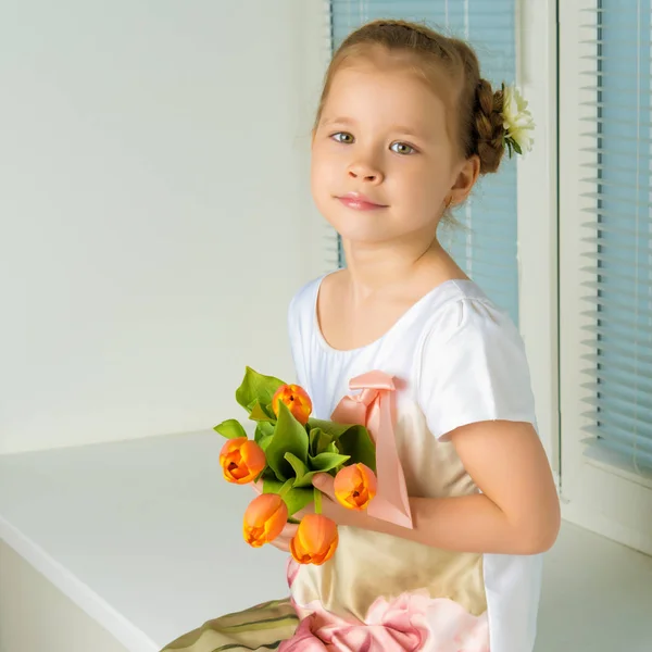 A little girl is sitting on the windowsill with a bouquet of tul — Stock Photo, Image