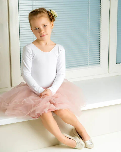 En liten flicka sitter vid fönstret med persienner — Stockfoto