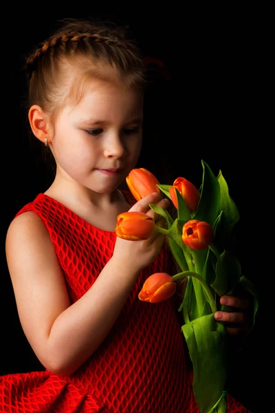 Kleines Mädchen mit einem Strauß Tulpen auf schwarzem Hintergrund. — Stockfoto
