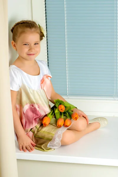 Маленькая девочка сидит на подоконнике с букетом тула — стоковое фото