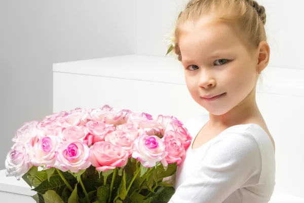 Little girl with a bouquet of flowers sits on a white staircase. — Stock Photo, Image