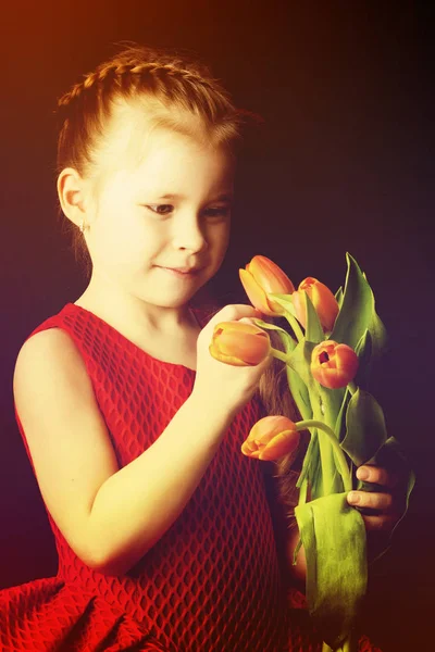 Little girl with a bouquet of tulips on a black background. — Stock Photo, Image