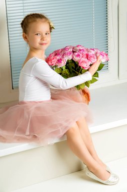 Küçük bir kız bir buket çiçek ile bir pencere pervazına oturur.