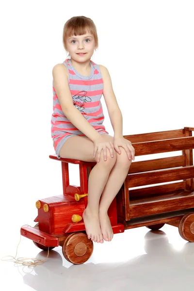 La chica está sentada en un gran coche de madera de juguete . —  Fotos de Stock