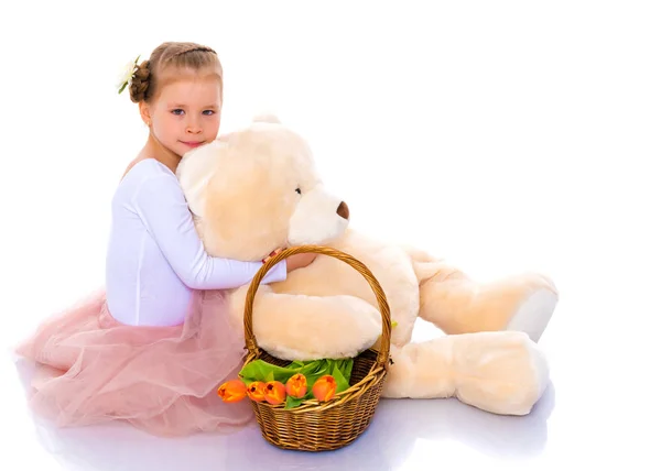 A little girl with a basket of flowers and a teddy bear is sitti — Stock Photo, Image