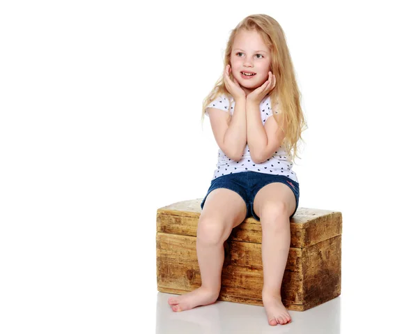 Uma menina está sentada em uma caixa de madeira . — Fotografia de Stock