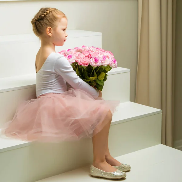 Kleines Mädchen mit einem Blumenstrauß sitzt auf einer weißen Treppe. — Stockfoto