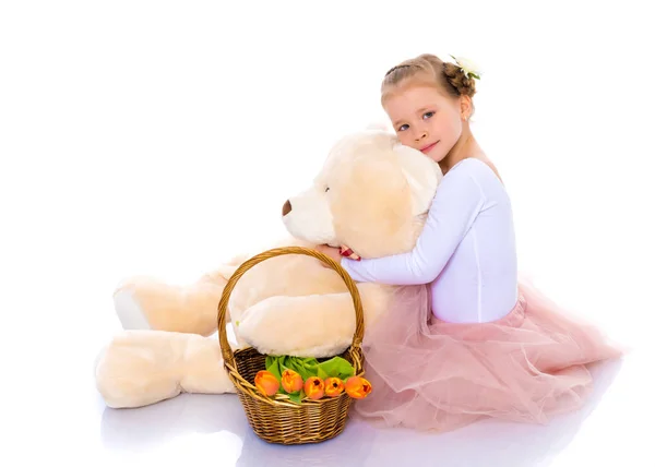 A little girl with a basket of flowers and a teddy bear is sitti — Stock Photo, Image