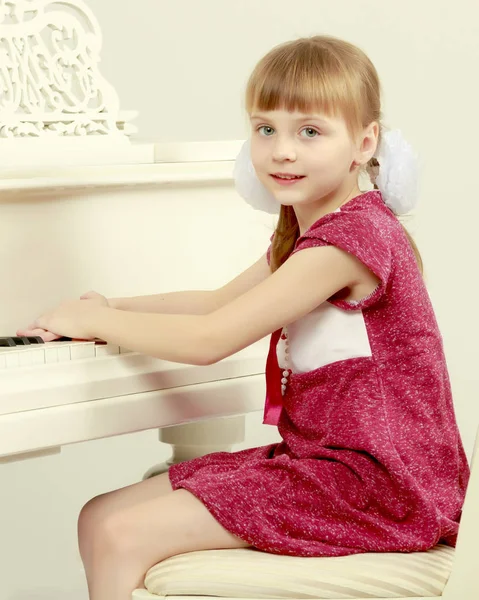 Uma menina está sentada na frente de um piano branco . — Fotografia de Stock